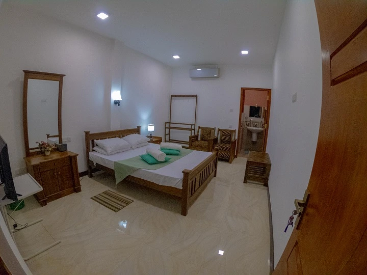 Deluxe Double Room 2 with a wooden double bed, wall-mounted air conditioning, television and the en-suite bathroom beyond