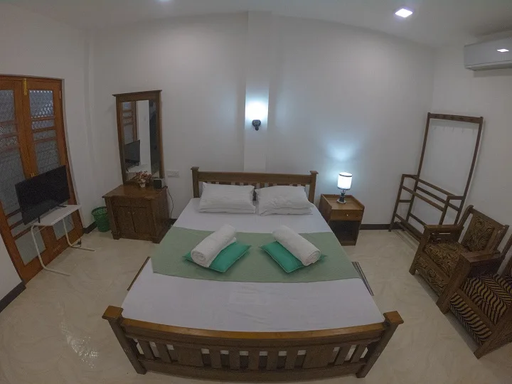 Deluxe Double Room 2 seen from the foot of the bed, with dressing mirror, television, bedside lamp and luggage rack