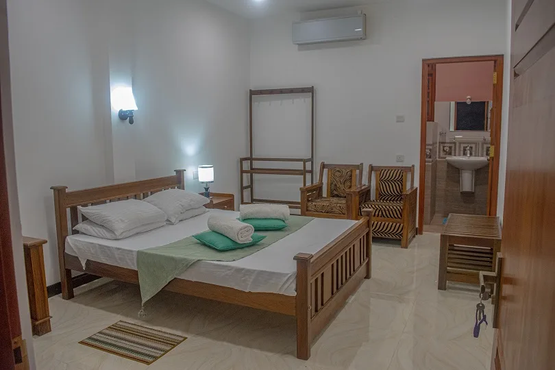 Deluxe Double Room 2 with a green bed runner, carved seating and the doorway through to the en-suite bathroom