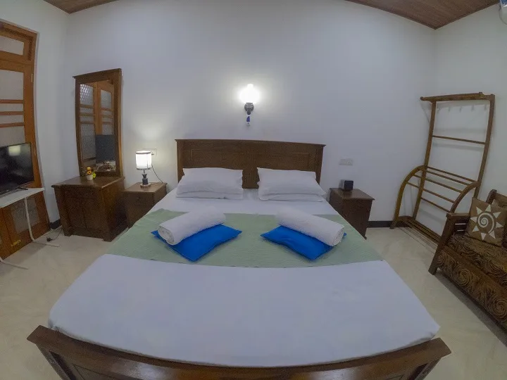 Deluxe Triple Room beds made up with folded towels and blue cushions, beside a bedside lamp and luggage rack